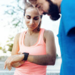 latina sportswoman and bearded sportsman looking together on smartwatch