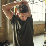 Close up of young sporty man in sportswear stretching his arm while standing at gym