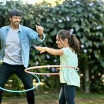 Laughing Father and Daughter Swinging Hoops in Backyard