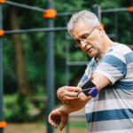 Active senior man exercising in nature, checking smart phone