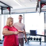 Overweight woman in gym training arms with trx fitness strips.