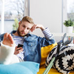 Young man with broken leg using smart phone at home