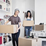 Lesbian couple carrying cardboard boxes in apartment