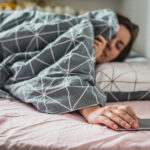 A young woman wakes up the bed. the alarm on the smartphone is ringing