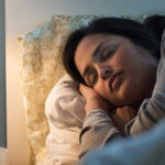 Woman sleepin in bed with side table lamp on