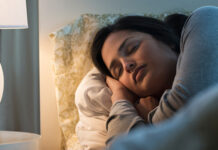 Woman sleepin in bed with side table lamp on