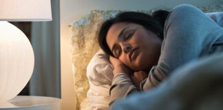 Woman sleepin in bed with side table lamp on