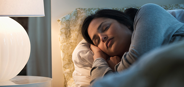 Woman sleepin in bed with side table lamp on