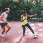 young sportsman and woman playing soccer on hardcourt