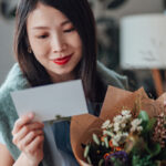 Femme tenant des fleurs et lisant une carte.