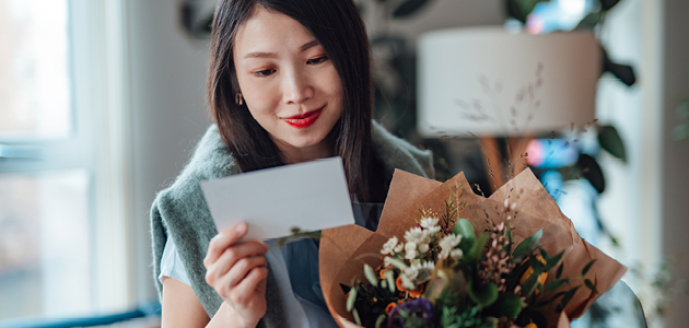 Femme tenant des fleurs et lisant une carte.