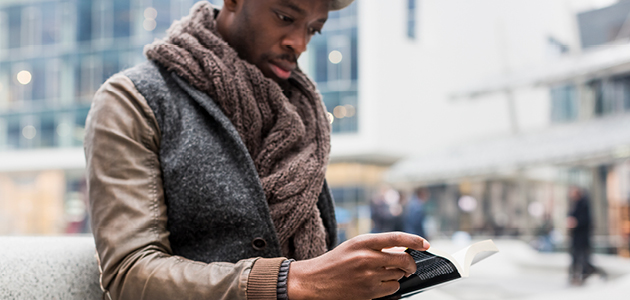 Homme assis à l'extérieur lisant un livre.