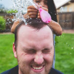 Girl popping water balloon on father’s head