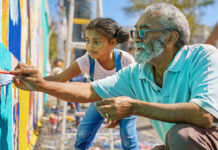 Older man and young girl painting a mural outside
