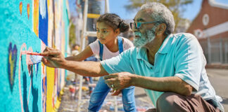 Older man and young girl painting a mural outside