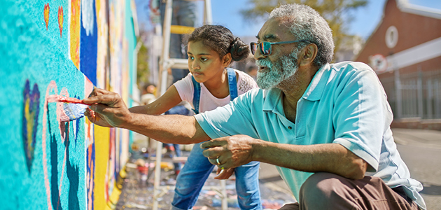 Older man and young girl painting a mural outside