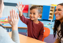 Garçon levant la main dans une salle de classe accompagné de sa mère et de son professeur