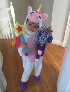 Evelyn Armstrong in a unicorn costume, holding a wand and a stuffed animal. 