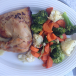 Roast chicken thigh and cooked broccoli, carrots and cauliflower on a plate