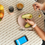 Woman eating avocado at table, with a bowl of fruit nearby