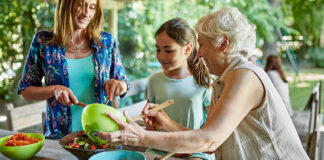 Grandmother, mother, and daughter make a salad together while sitting at a table in the backyard