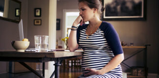 Pregnant woman sitting at desk looking at the computer screen, with a serious expression on her face