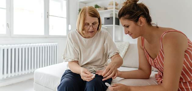 Older woman helps younger woman check insulin levels using a fingerstick