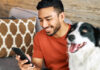 Man looking at mobile phone in his right hand with dog beside him