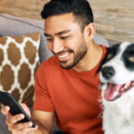 Man looking at mobile phone in his right hand with dog beside him