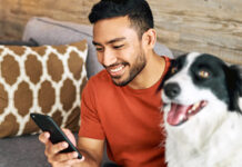 Man looking at mobile phone in his right hand with dog beside him