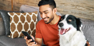 Man looking at mobile phone in his right hand with dog beside him