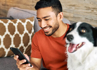 Man looking at mobile phone in his right hand with dog beside him